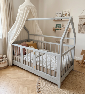 Szare drewniane łóżko domek Montessori dla dziecka z bezpiecznymi szczebelkami i otwieraną bramką w przytulnej aranżacji pokoju dziecięcego.
