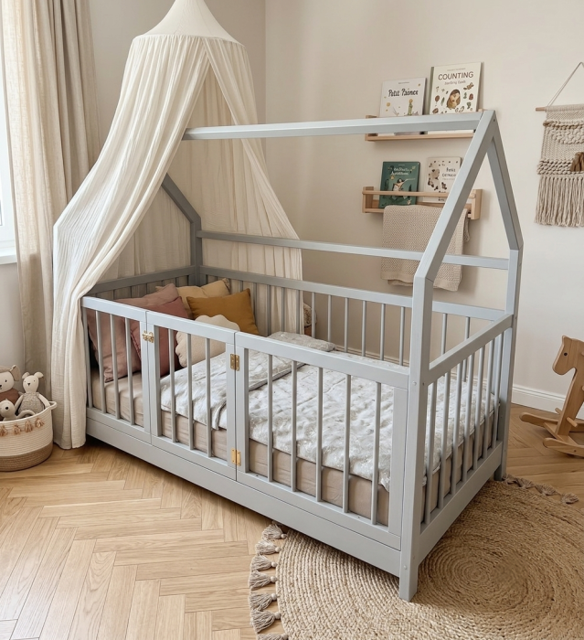 Szare drewniane łóżko domek Montessori dla dziecka z bezpiecznymi szczebelkami i otwieraną bramką w przytulnej aranżacji pokoju dziecięcego.